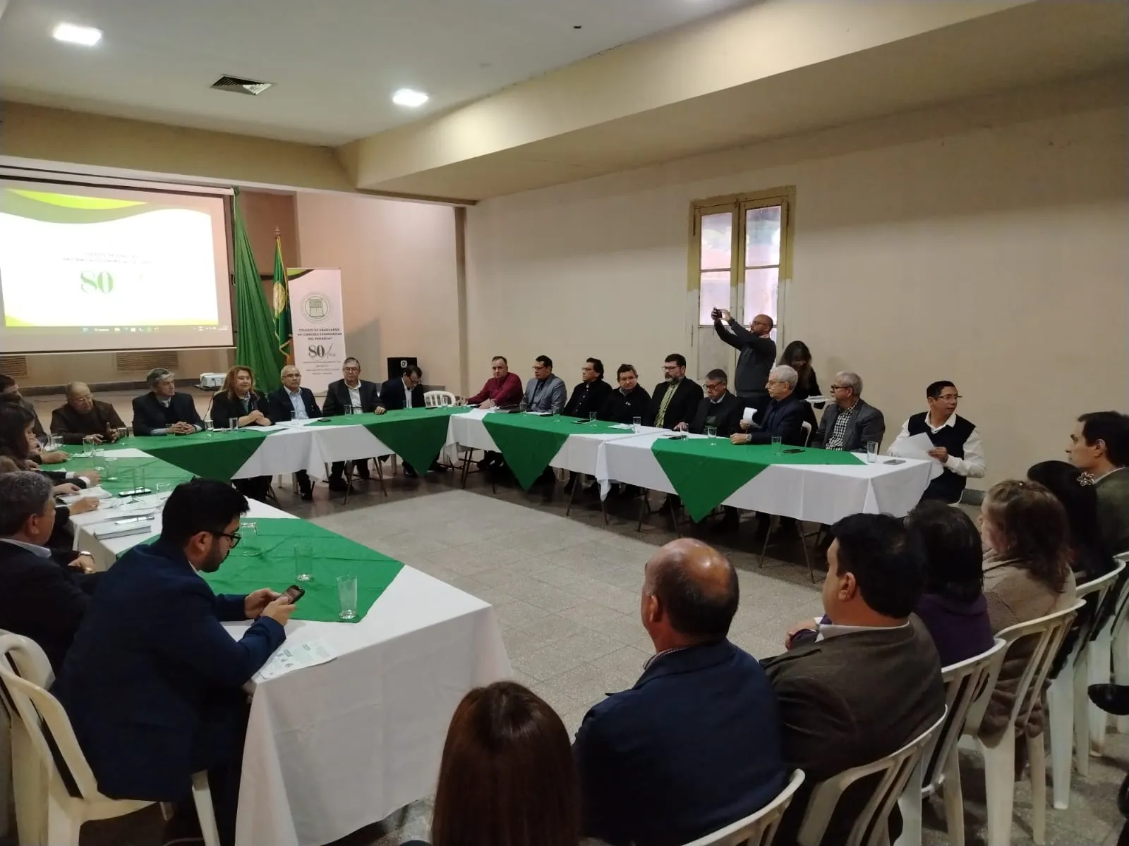 Asistentes sentados alrededor de la mesa en U del salón durante el acto de lanzamiento