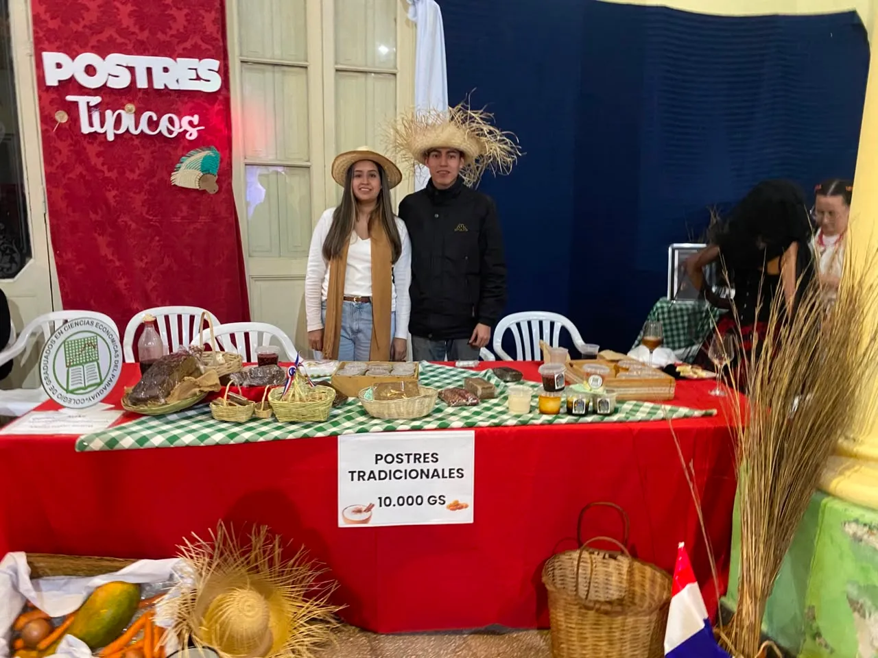Puesto de postres típicos atendido por dos jóvenes, con dulces tradicionales sobre la mesa